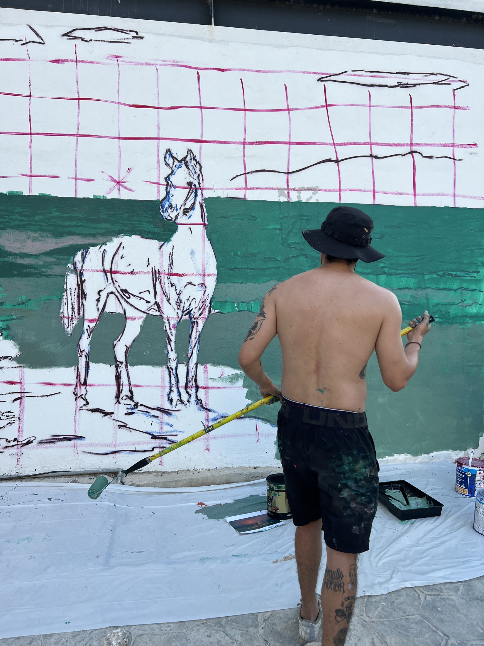 Artista pinta el fondo verde junto al boceto de un caballo trazado sobre una cuadrícula