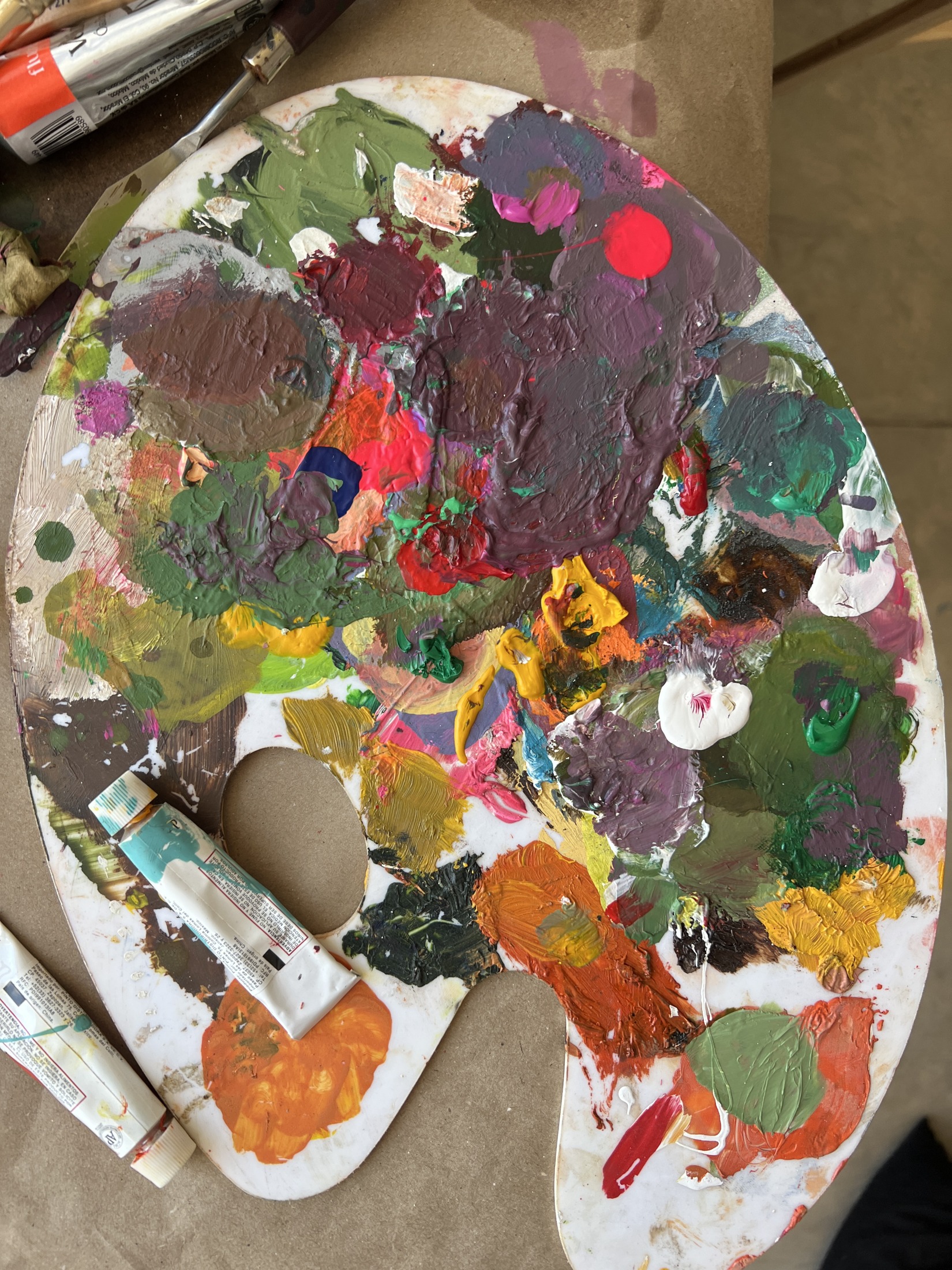 Paleta de pintor cubierta de colores con tubos de óleo